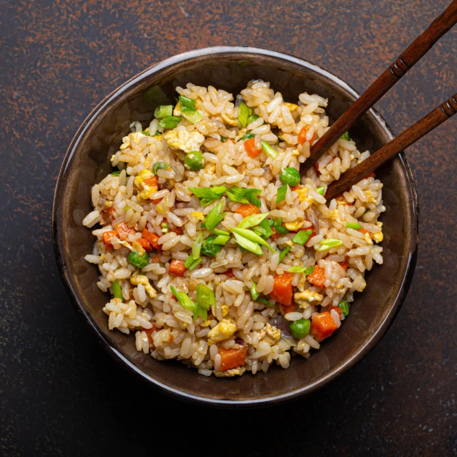 A bowl of fried rice with spring onions and chopsticks.
