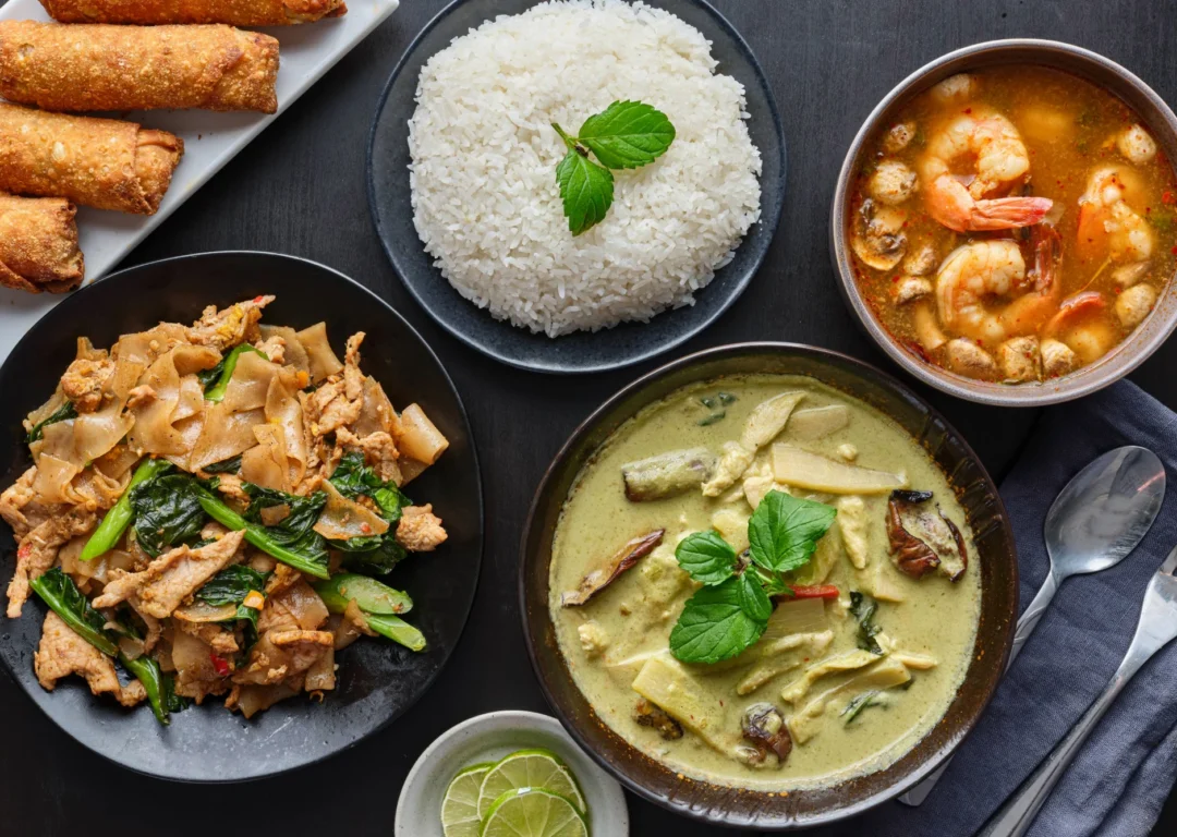 A selection of classic Thai dishes on a black table.